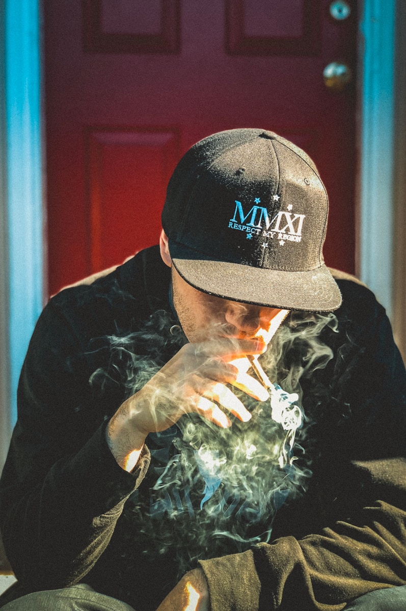man in black cap and shirt sitting near door while smoking